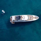 Luxuriöse weiße Yacht mit zwei kleinen Booten im klaren blauen Wasser, von oben fotografiert, Ruhe und Komfort an Bord.