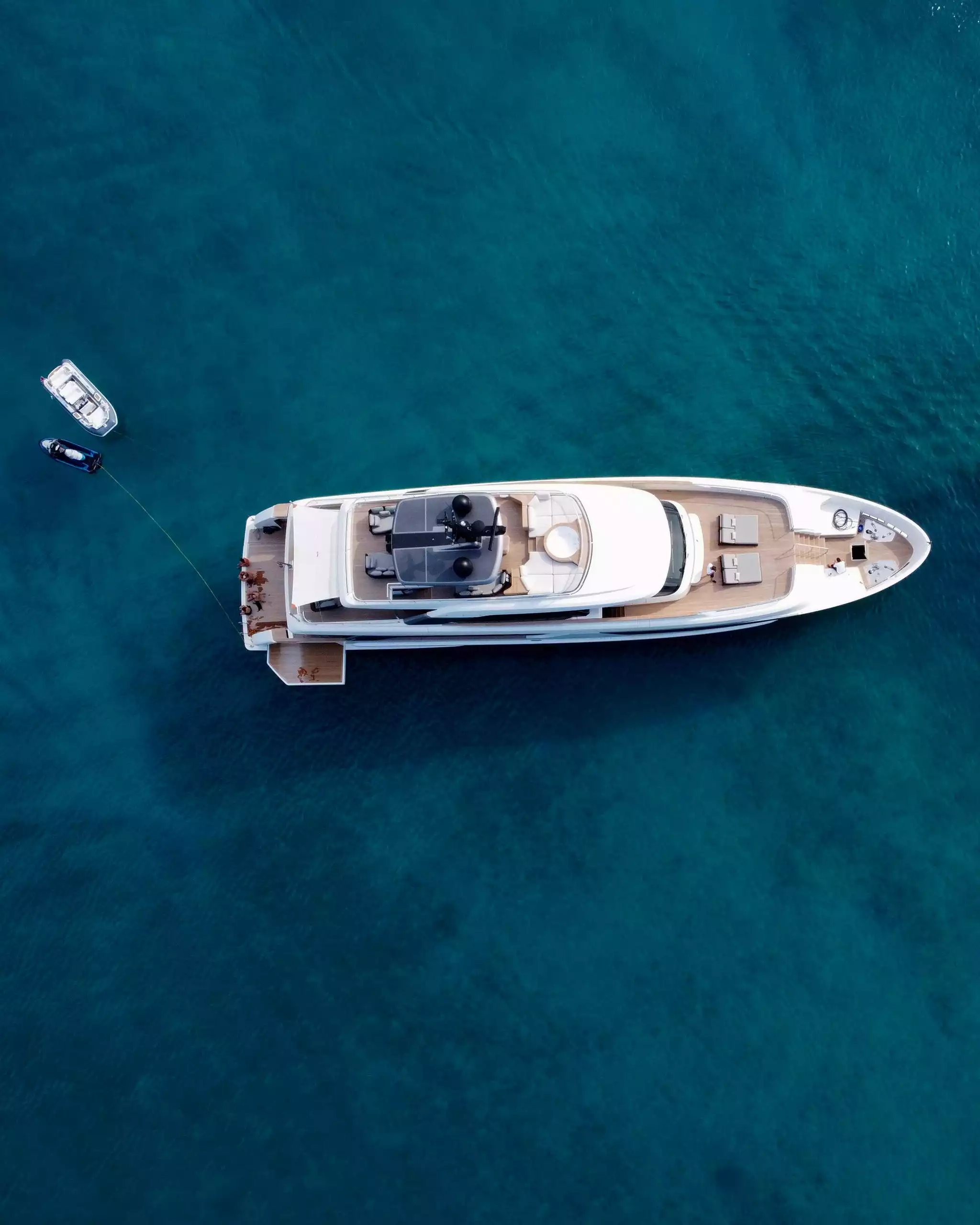 Luxuriöse weiße Yacht mit zwei kleinen Booten im klaren blauen Wasser, von oben fotografiert, Ruhe und Komfort an Bord.