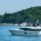 Weiße Yacht ankert ruhig vor bewaldeter Felseninsel im blauen Meer bei klarem Himmel