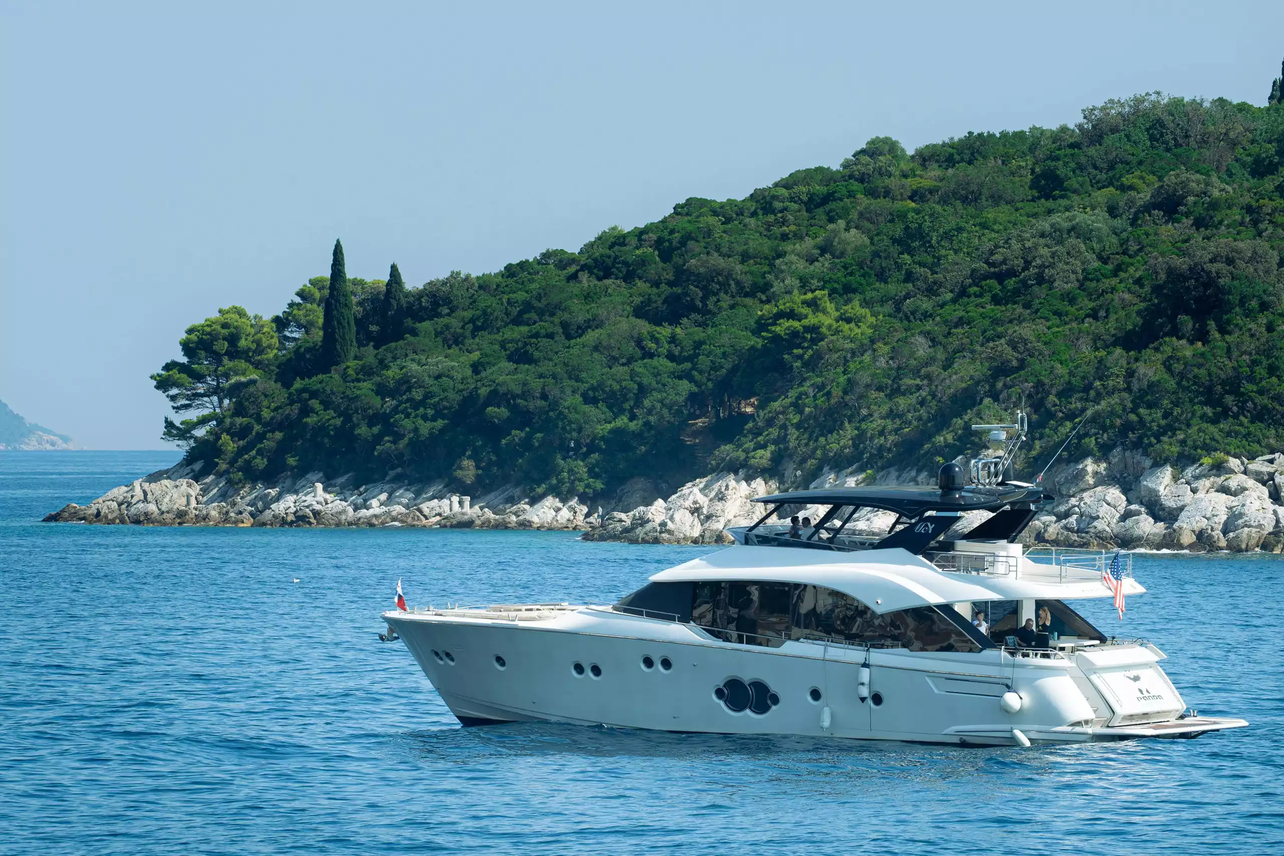 Weiße Yacht ankert ruhig vor bewaldeter Felseninsel im blauen Meer bei klarem Himmel